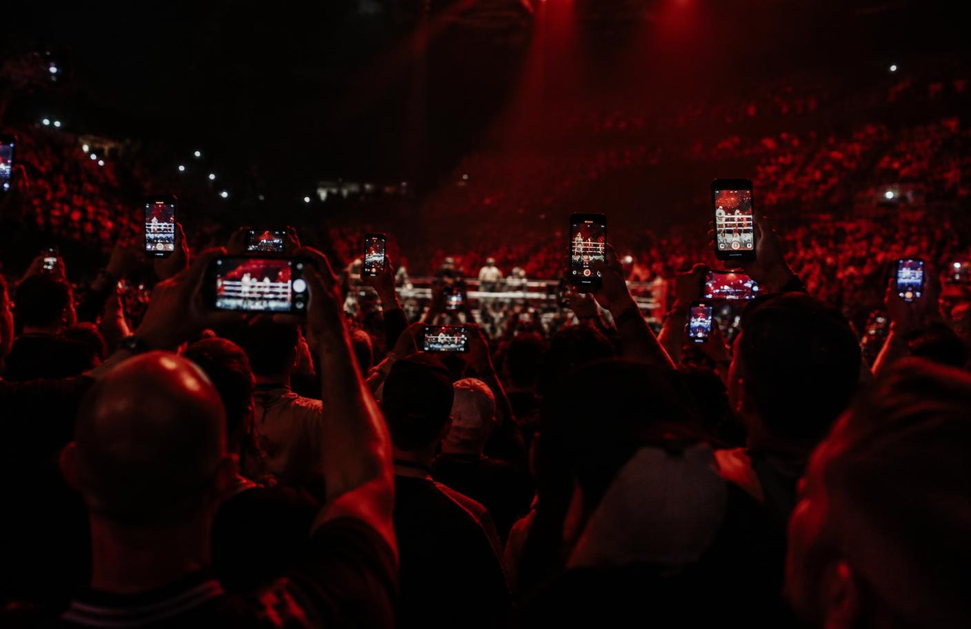 Boxing crowd filming the ring on their phones under red arena light